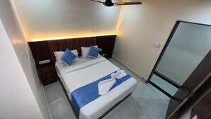 A hotel room with a bed, bedside tables, a mirror, and a ceiling fan. - hotel surya grand (Mumbai)