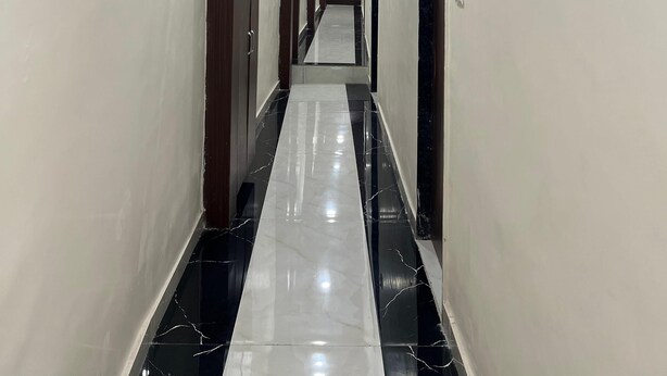 A long, narrow hallway with white walls, wooden paneling on the ceiling, and a black and white marble floor. - hotel surya grand (Mumbai)