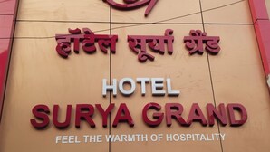 A sign for Surya Grand Hotel with the text "Feel the warmth of hospitality" and a logo above the name. - hotel surya grand (Mumbai)