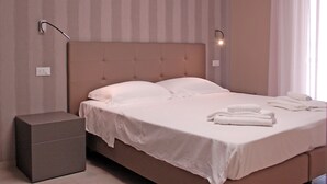 A neatly made bed with white linens and pillows, a bedside table, and a wall-mounted light fixture. - Marconi Seaside Residence Pool Wifi  (Alba Adriatica)