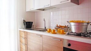 A modern kitchen with white cabinets, a stainless steel sink, and a pot of spaghetti on the stove. - Marconi Seaside Residence Pool Wifi  (Alba Adriatica)