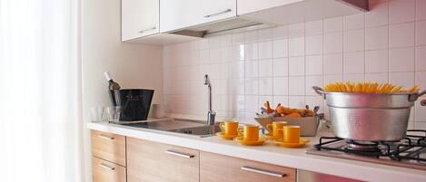 A modern kitchen with white cabinets, a stainless steel sink, and a pot of spaghetti on the stove.