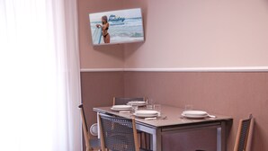 A dining area with a table set for four, chairs, and a television displaying a holiday advertisement. - Marconi Seaside Residence Pool Wifi  (Alba Adriatica)