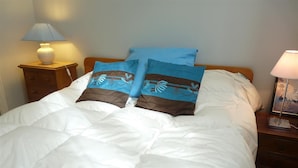 Un lit bien fait, avec une literie blanche et deux coussins décoratifs aux motifs bleus et bruns.