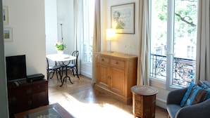 Un salon comprenant un meuble en bois, une petite table ronde, un canapé, une table à manger avec des chaises et un téléviseur posé sur un meuble en bois.