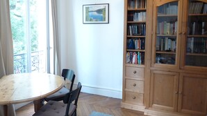 Une pièce avec une table et des chaises en bois, une bibliothèque et une fenêtre avec des rideaux.