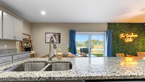Una cocina moderna con encimeras de granito, electrodomésticos de acero inoxidable y vistas a un balcón con pared verde y un letrero de neón.