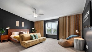 Un dormitorio moderno con una cama, un sofá, una mesita auxiliar, un ventilador de techo y una ventana con persianas.