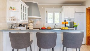 Une cuisine moderne avec des meubles blancs, un îlot central doté de tabourets et un four encastré.