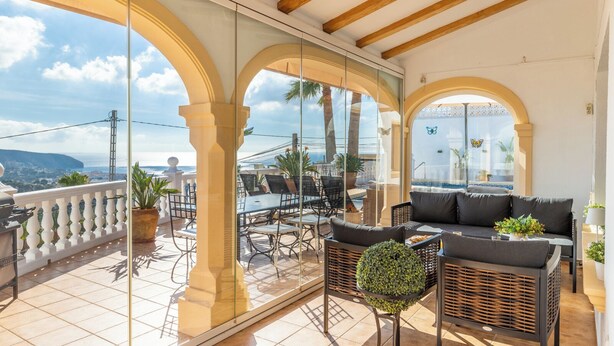 Une terrasse extérieure ensoleillée, dotée d’un espace repas, de sièges et offrant une vue sur la mer.