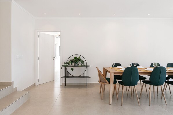 A modern dining area with a wooden table and chairs, a potted plant, and a staircase leading to another room.