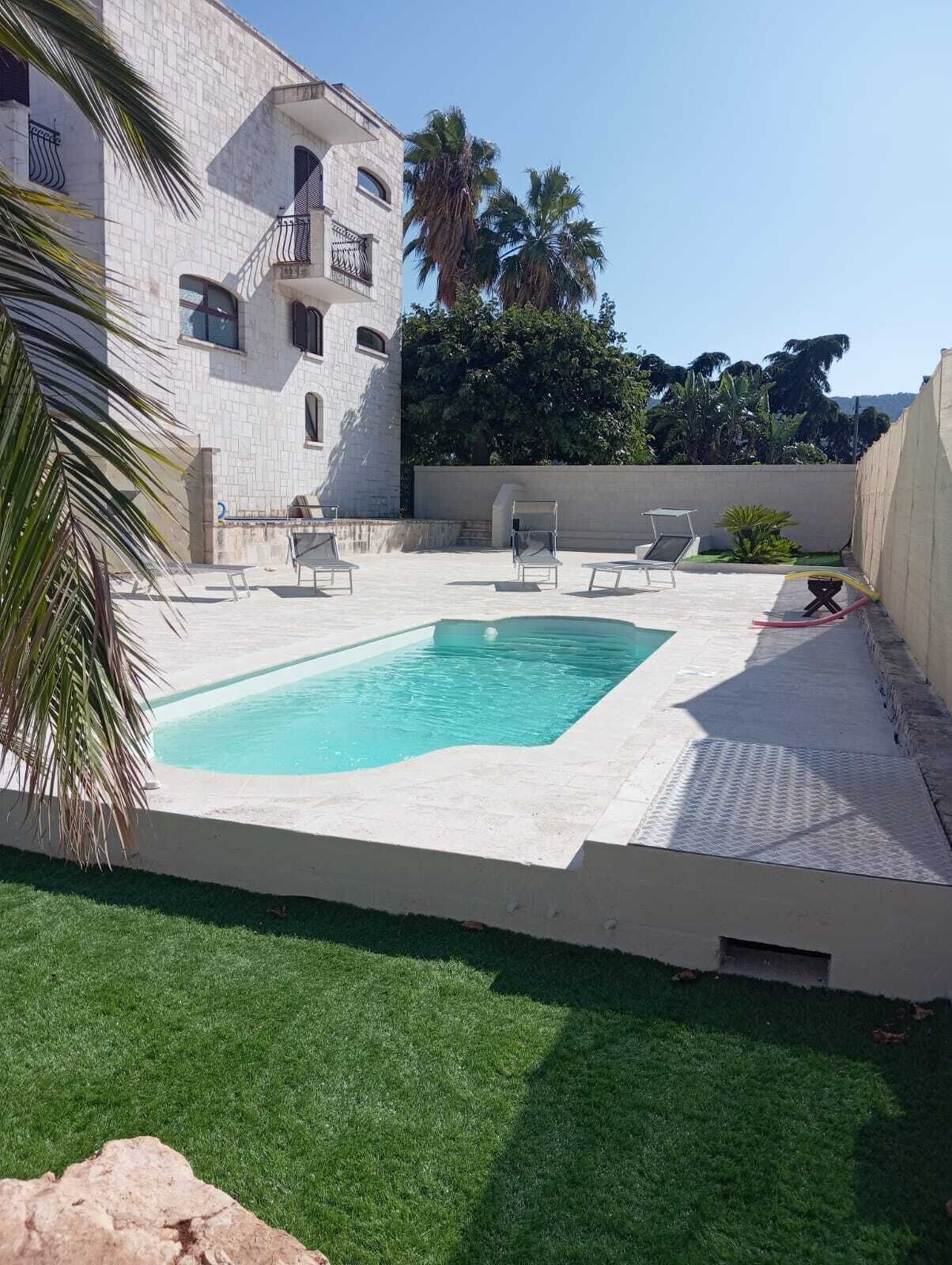A swimming pool with a tiled deck, surrounded by a grassy area and a building with a stone facade.