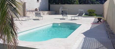 A swimming pool with a tiled deck, surrounded by a grassy area and a building with a stone facade.