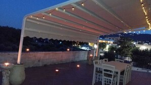 An outdoor patio area with a table and chairs under a canopy, string lights, and a view of the city at dusk. - La Mery Giò House (Fasano)