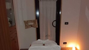 A room with a bed, a wooden wardrobe, a mirror, a curtain, and a small table with a lamp. - La Mery Giò House (Fasano)