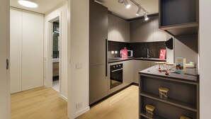 A modern kitchen with built-in appliances, a microwave, and a sink. There are wooden cabinets and a countertop with a microwave and a kettle. - Waterfront Seaside in Genova (Genoa)