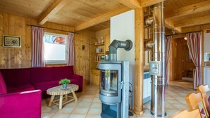 Un interior acogedor de cabaña con paredes de madera, un sofá, una mesita con una planta, un estufa de leña y una chimenea.