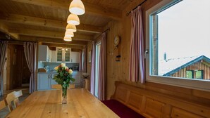 Un interior de madera con una mesa de comedor, un jarrón de flores y un ventanal con cortinas.