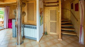 Un interior de madera con una caldera central, una escalera y una puerta con un panel decorativo.