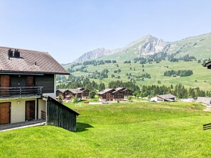 Un village de montagne isolé, avec ses maisons traditionnelles en bois, un paysage verdoyant au premier plan et, en arrière-plan, des montagnes aux reliefs accidentés.