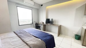 Una camera d'albergo con un letto, una scrivania con televisore, una finestra e vista sulla città.