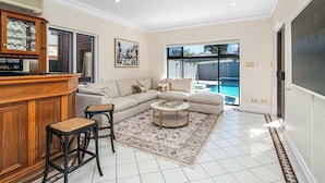 A living room with a sectional sofa, a coffee table, and a bar area with stools. - 6BR Lower Mitcham home, pool, cinema, near CBD (Lower Mitcham)