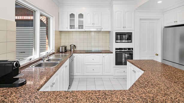 A modern kitchen with white cabinets, granite countertops, stainless steel appliances, and a window with blinds. - 6BR Lower Mitcham home, pool, cinema, near CBD (Lower Mitcham)