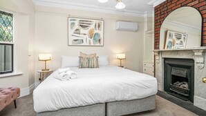 A bedroom with a large bed, two bedside tables with lamps, a fireplace, and artwork on the walls. - 6BR Lower Mitcham home, pool, cinema, near CBD (Lower Mitcham)