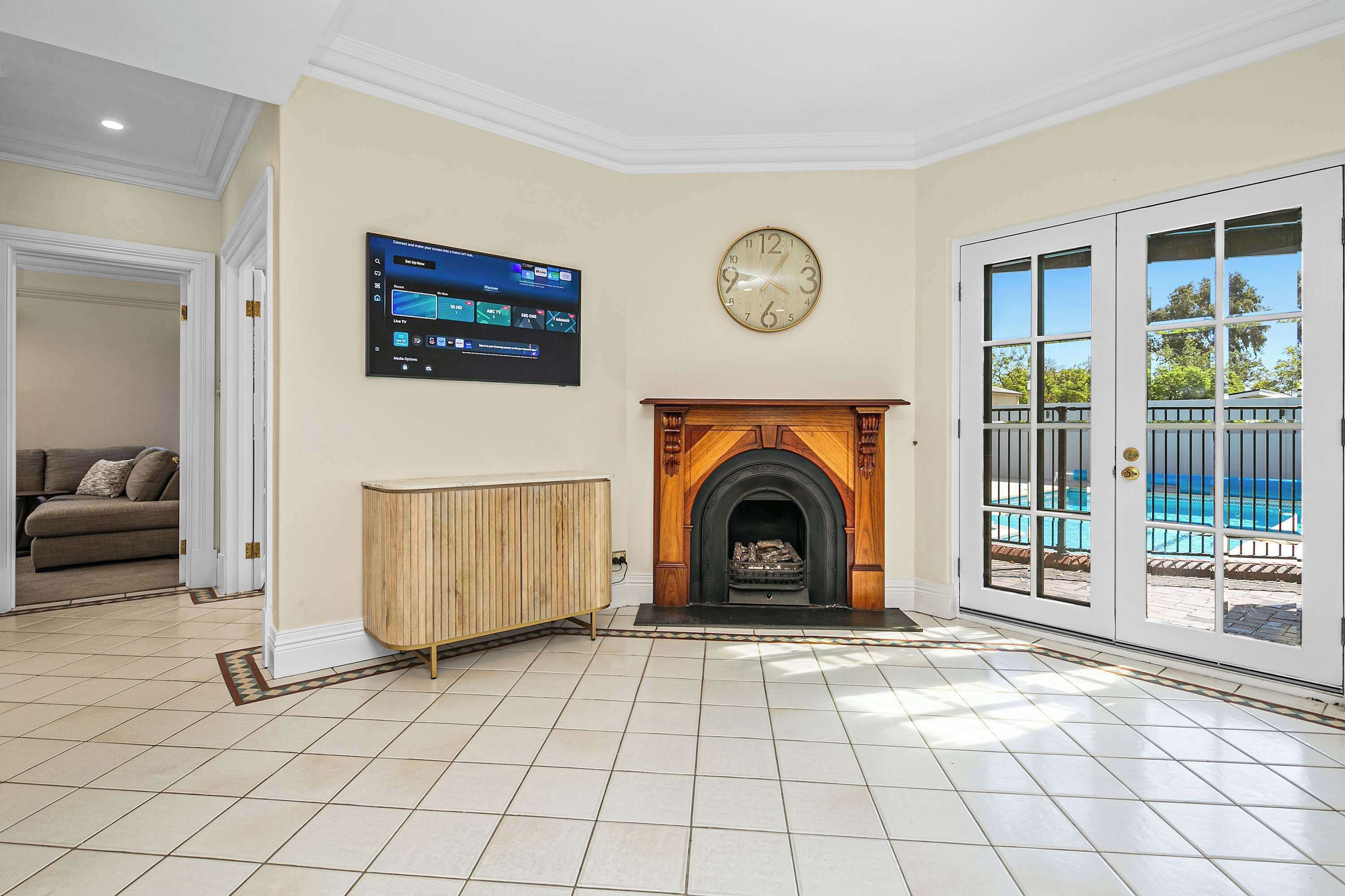 A living room with a fireplace, a television mounted on the wall, and a view of a pool through a glass door.