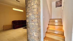 A staircase with wooden steps leading up to a landing, a stone wall, a brown leather sofa, and a light fixture on the ceiling. - Kuća za odmor Fay (Crikvenica)