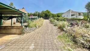 A paved pathway leading uphill with a covered area on the left and a white building on the right. - Kuća za odmor Fay (Crikvenica)