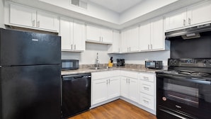 A modern kitchen with white cabinets, a black refrigerator, a microwave, a coffee maker, and a stove.