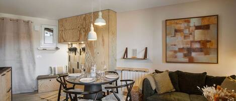 A modern living room with a round dining table, black chairs, a green sofa, and a large abstract painting.