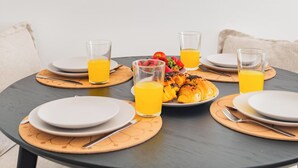 A round dining table with plates, cutlery, and glasses of orange juice. - Seaside Modern Flat II at Cascais (Cascais)