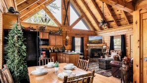 A cozy cabin interior with a dining area, kitchen, fireplace, and a bear statue.