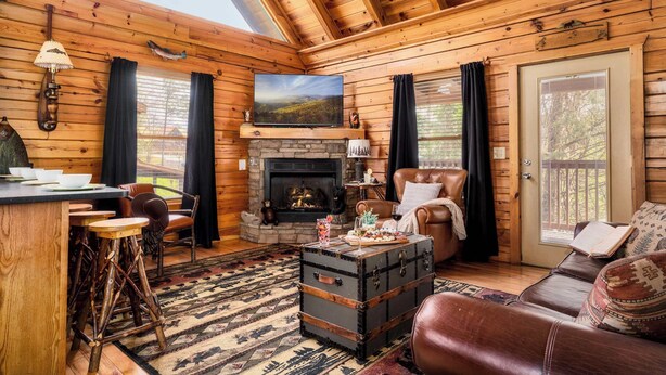 A cozy log cabin interior with a fireplace, leather furniture, and a rustic dining area.