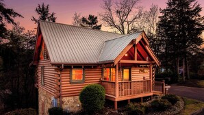 A log cabin with a metal roof, wooden deck, and a stone foundation.