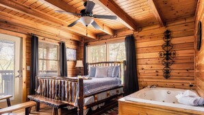 A wooden cabin bedroom with a bed, a bench, a bathtub, and a ceiling fan.