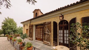 A courtyard with a cobblestone path, potted plants, a table with a chair, and a building with arched windows and a brick chimney. - Castello di Casalborgone - Luxury Castle (Casalborgone)