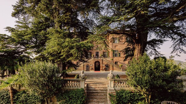 A historic building with a central staircase leading to a red door, surrounded by lush greenery and a gravel pathway. - Castello di Casalborgone - Luxury Castle (Casalborgone)