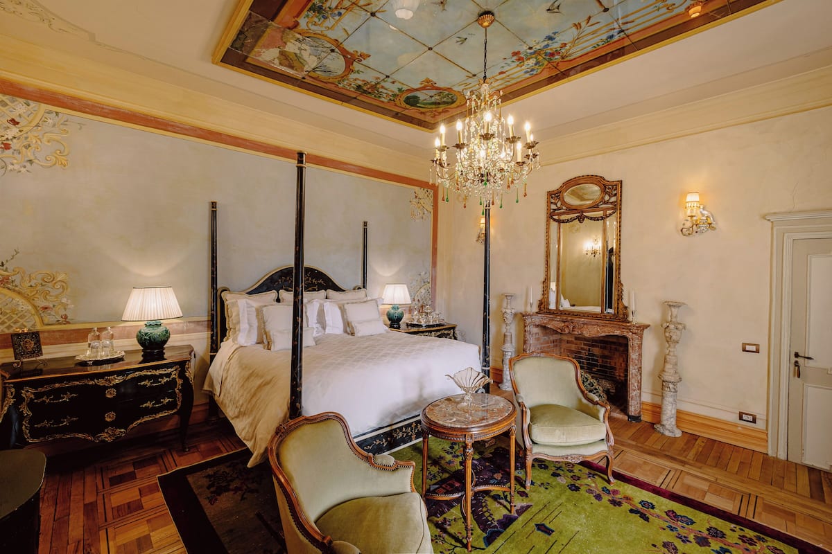 Ein luxuriöses Schlafzimmer mit einem Himmelbett, einer Kristallleuchter, einem Spiegel und einem Kamin.