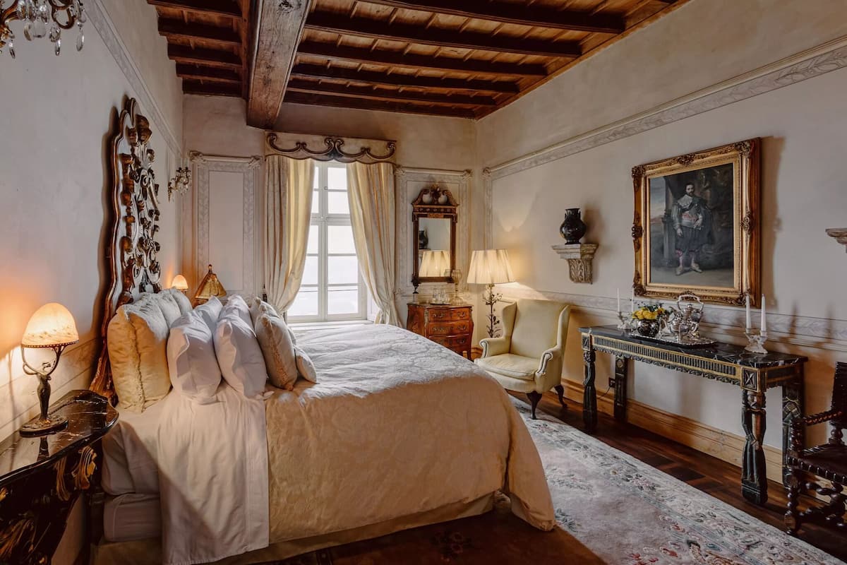 Ein klassisches Schlafzimmer mit einem großen Bett, einer Holzzieldecke, einem Spiegel, einem Tisch mit einer Vase und einem Gemälde an der Wand.