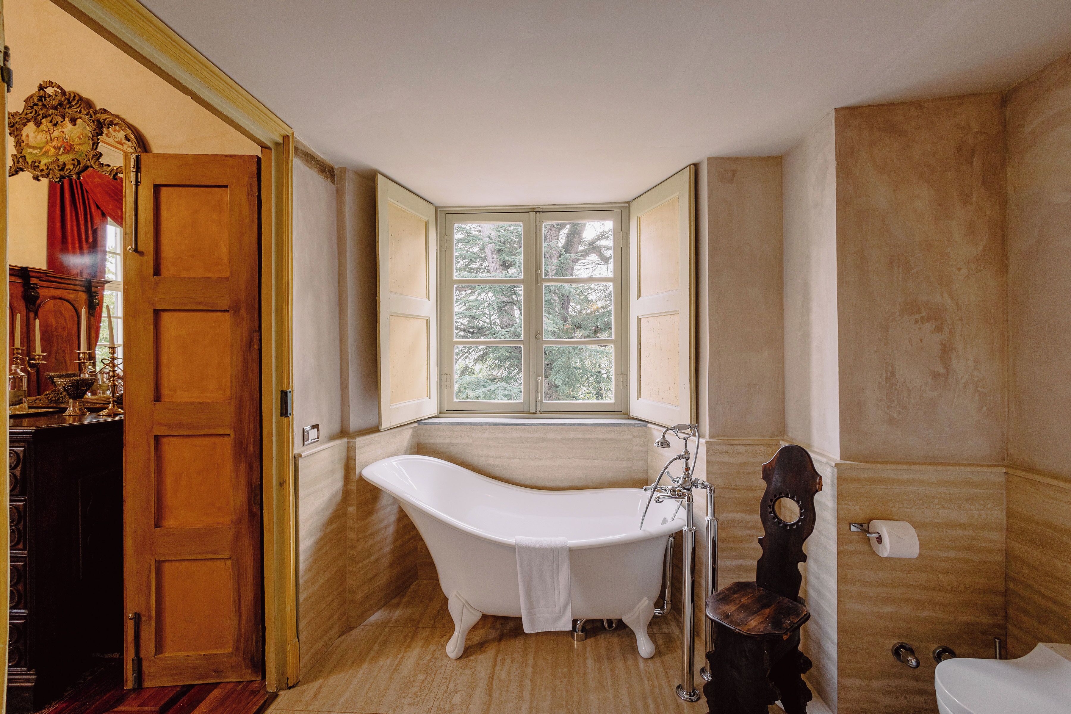 A bathroom with a freestanding bathtub, a window, and a wooden door.