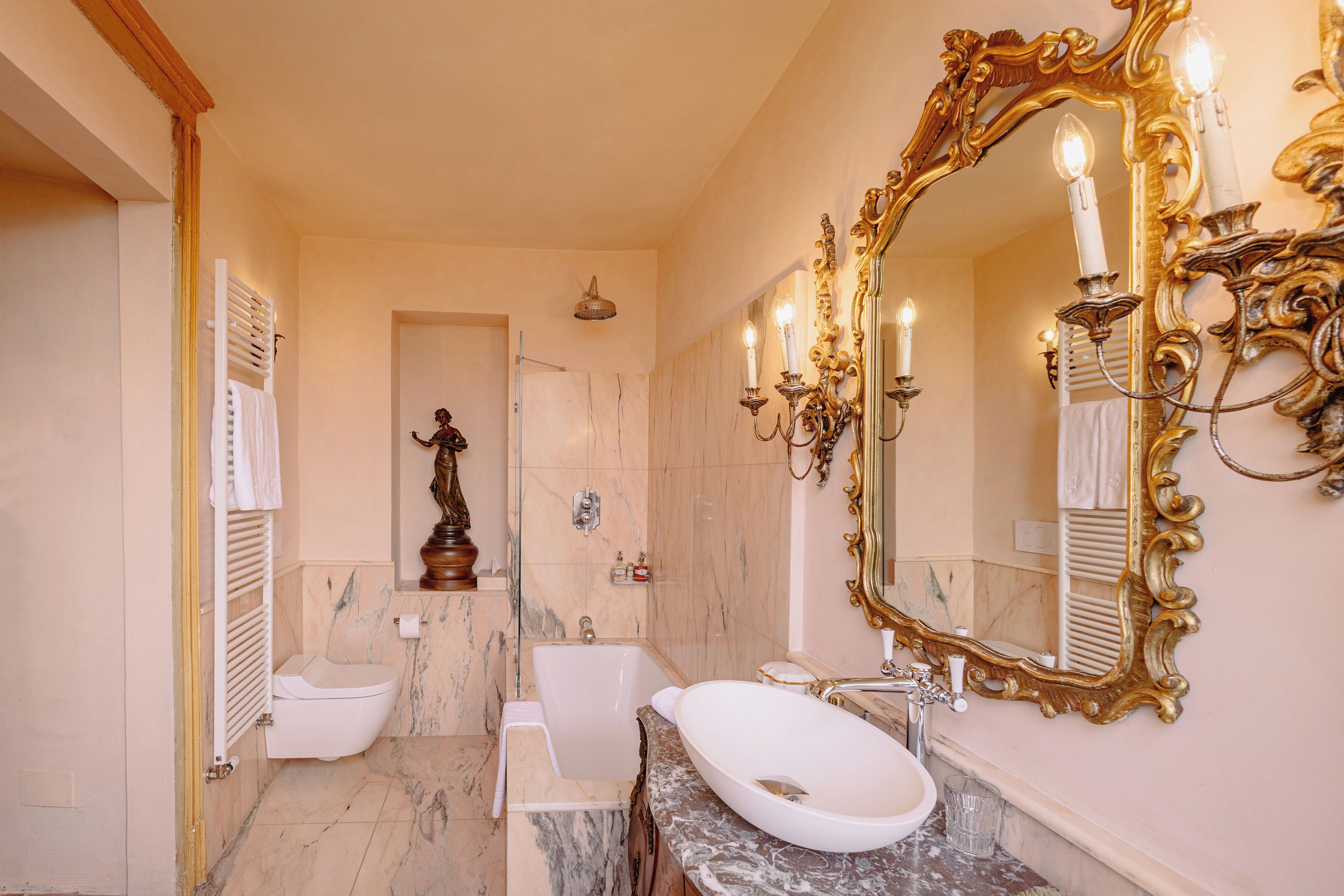 A bathroom with a bathtub, a sink, a large ornate mirror, and a statue.