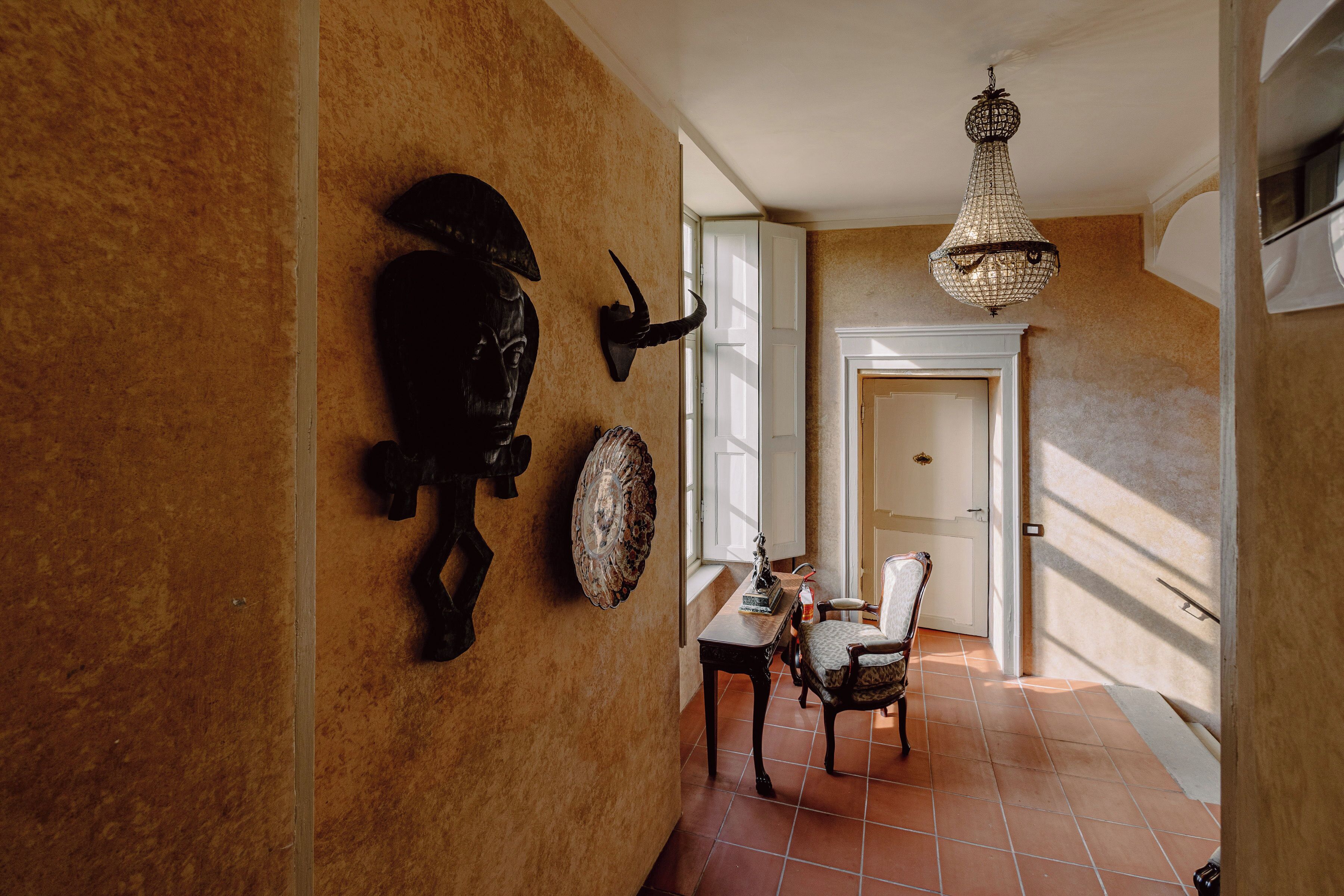 A hallway with a rustic wall, a chandelier, and a dining area with a table and chairs.