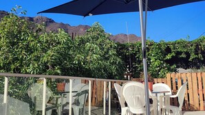 An outdoor patio with a table and chairs, a metal umbrella, and a view of mountains.