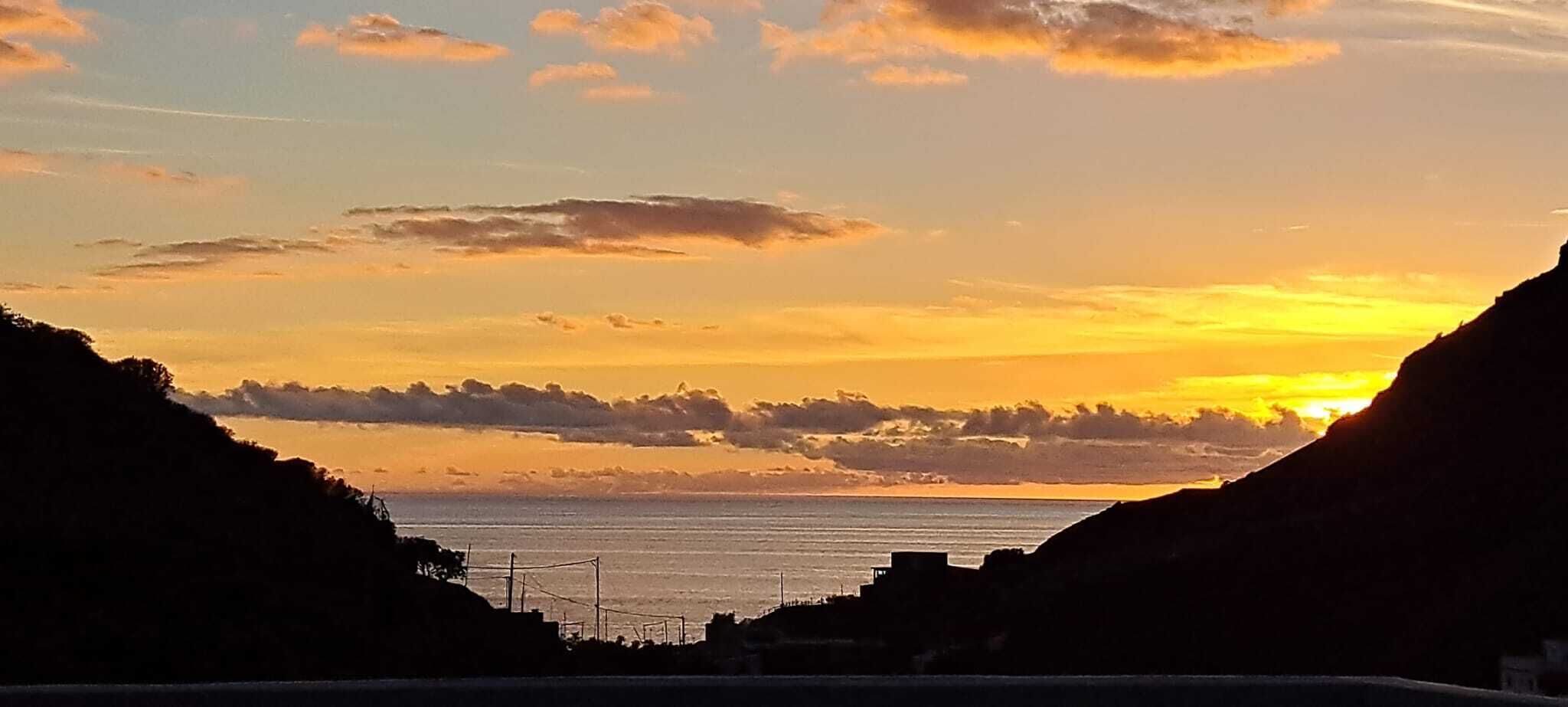 A coastal sunset view with a silhouette of hills and a clear sky.