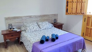 A bedroom with a bed, wooden headboard, nightstands, a purple bedspread, and a wooden wardrobe.