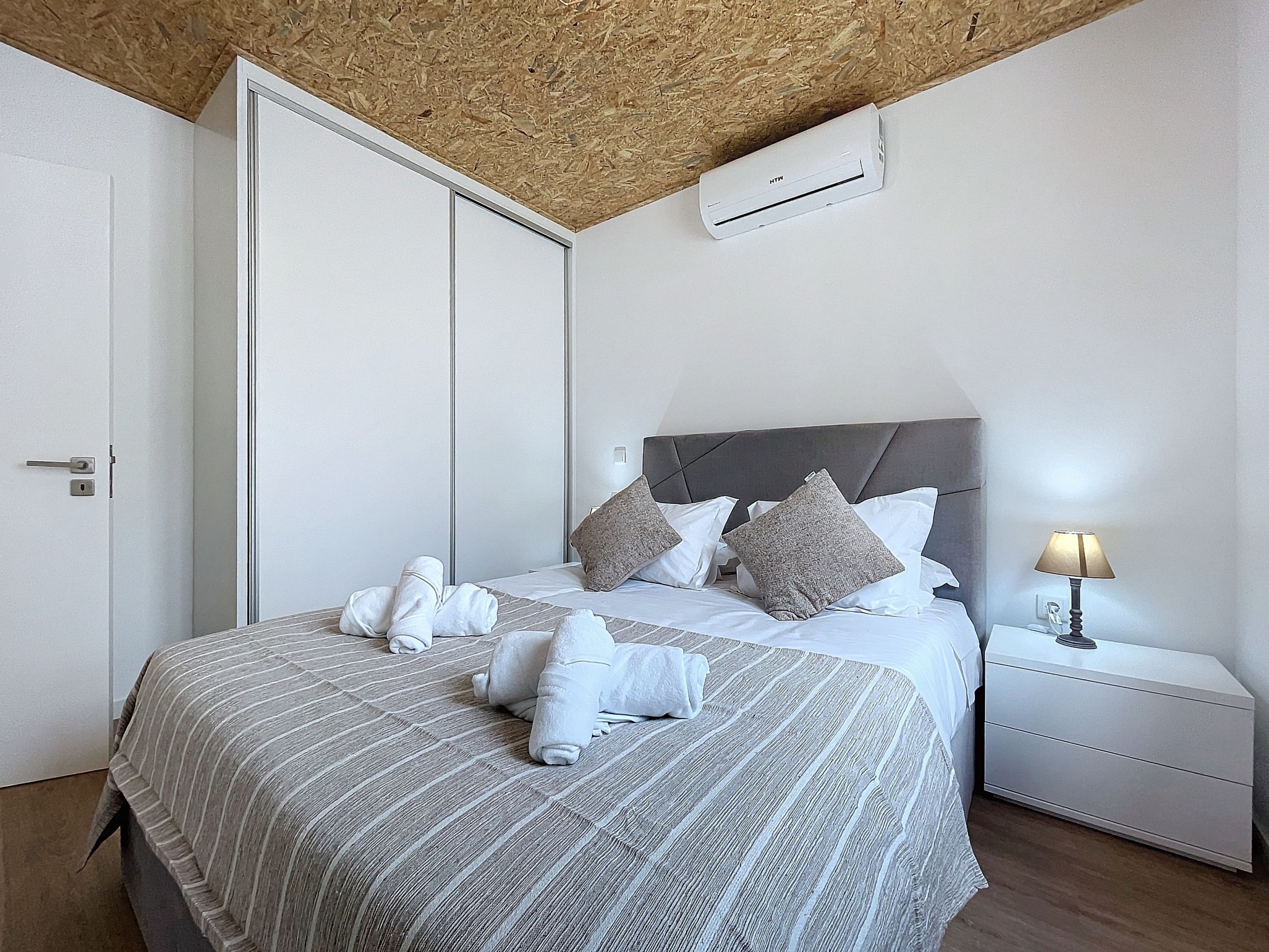 A neatly made bed with towels, a bedside lamp, and a wall-mounted air conditioner.