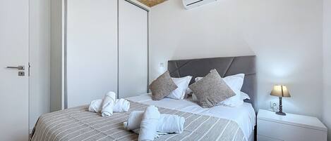 A neatly made bed with towels, a bedside lamp, and a wall-mounted air conditioner.